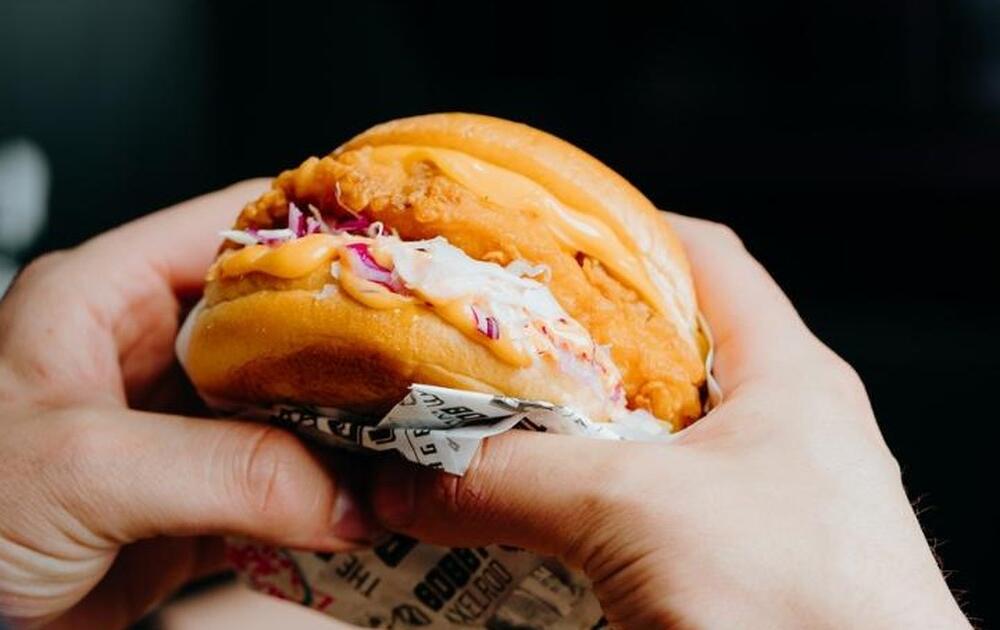 Hands holding a crispy chicken burger, the cheat meal Geelong lifters ask about at Carbon Gym