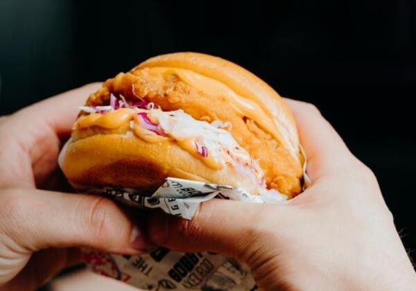 Hands holding a crispy chicken burger, the cheat meal Geelong lifters ask about at Carbon Gym