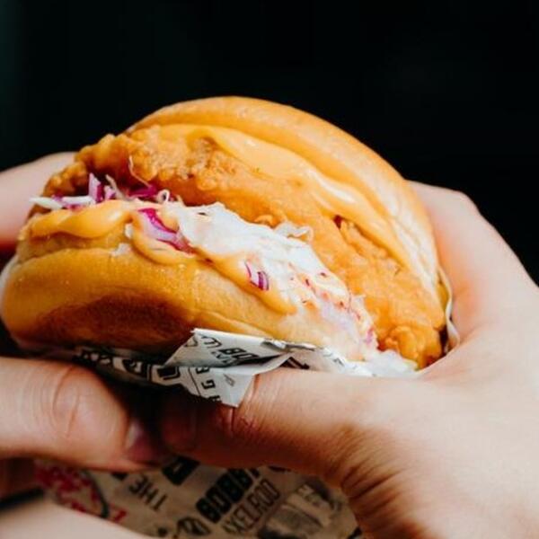 Hands holding a crispy chicken burger, the cheat meal Geelong lifters ask about at Carbon Gym