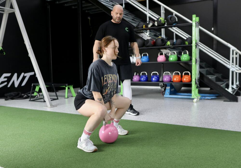 Member doing a kettlebell squat on the turf with a coach supervising during personal training at Carbon Gym Geelong