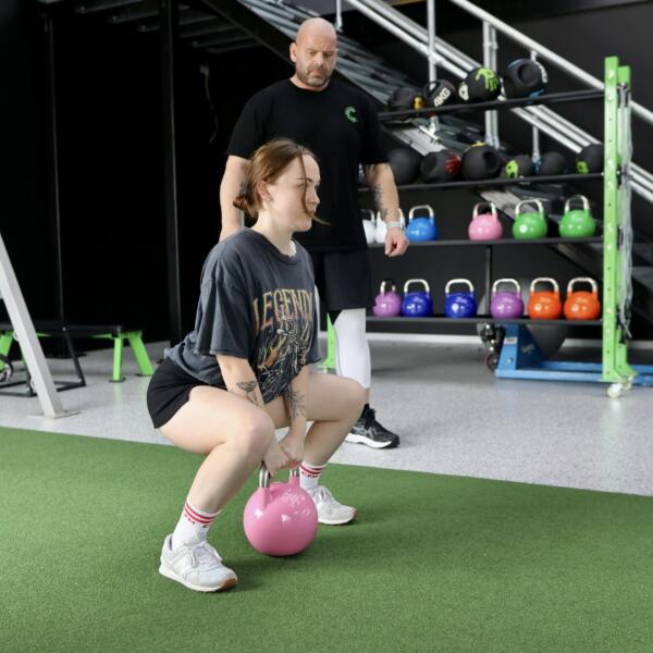 Member doing a kettlebell squat on the turf with a coach supervising during personal training at Carbon Gym Geelong
