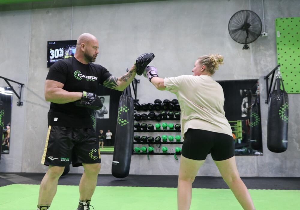 Boxing vs boxfit at Carbon Gym: coach holding focus mitts for a woman throwing a punch