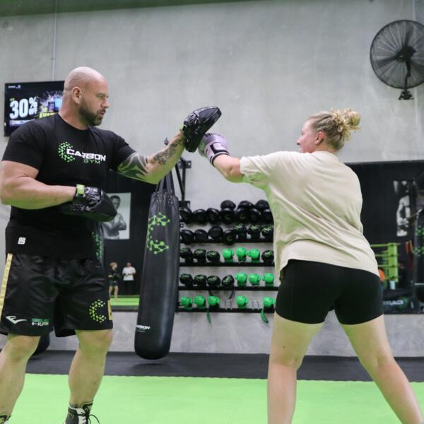 Boxing vs boxfit at Carbon Gym: coach holding focus mitts for a woman throwing a punch