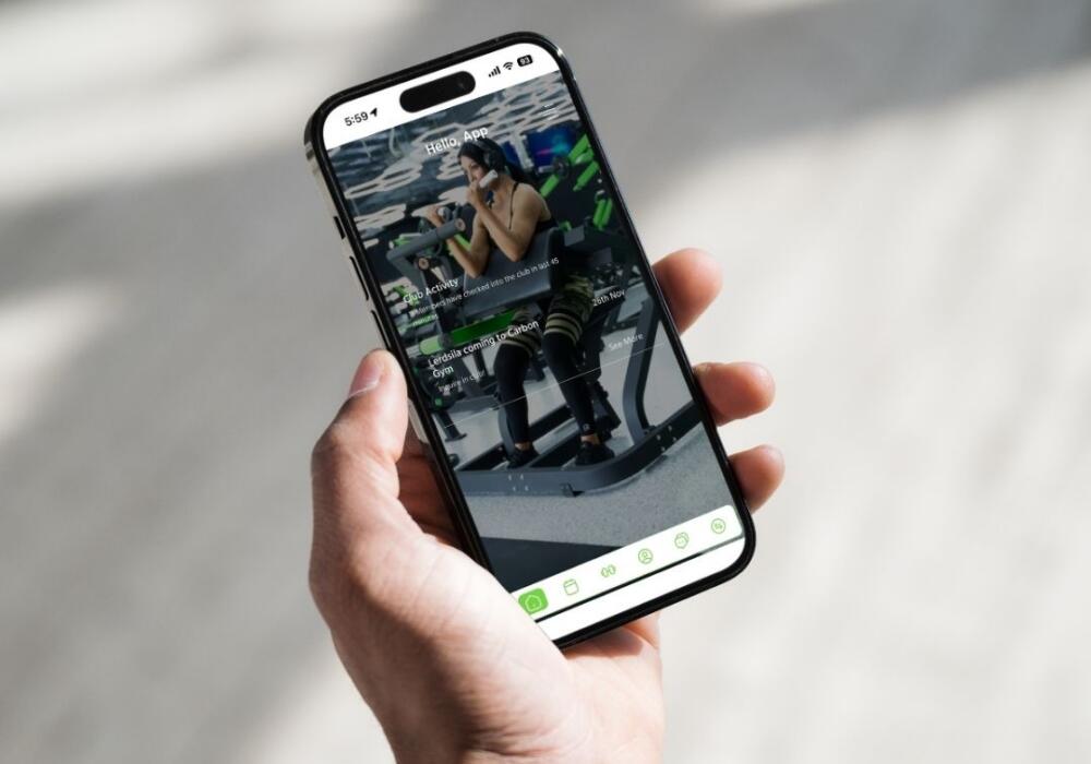 Hand holding a phone showing the Carbon Gym member app with club activity and news at Carbon Gym Geelong