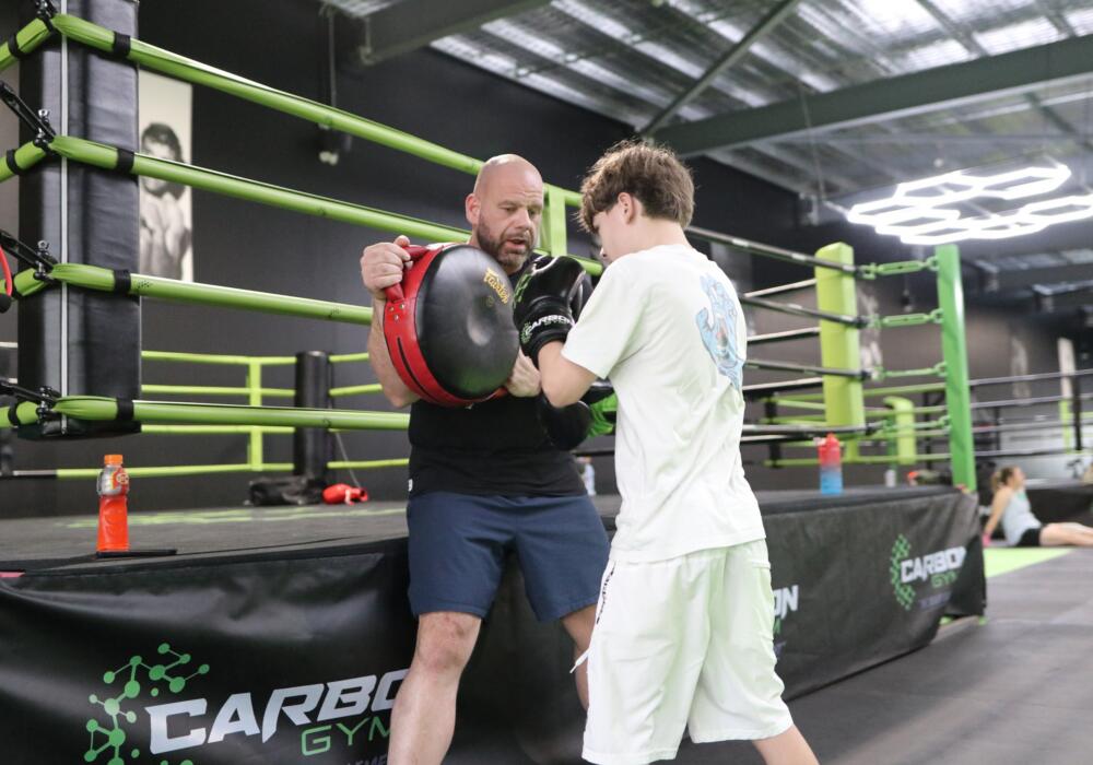 Coach holding focus pads for a teenage boxer in the ring during a teen boxing class at Carbon Gym Geelong