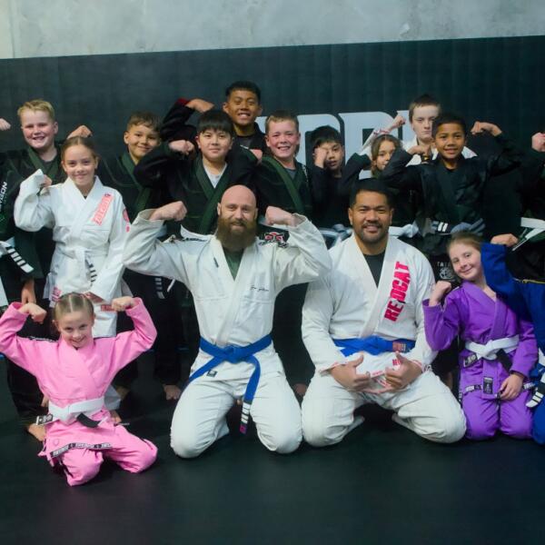 Kids BJJ class group photo with coaches at Carbon Gym Geelong, students in gis flexing and smiling