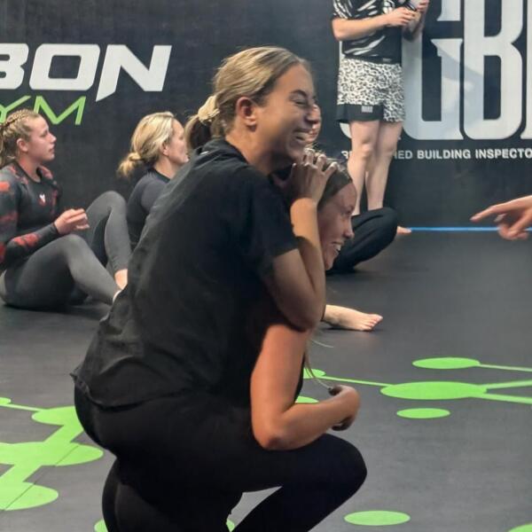 Women laughing during a Brazilian Jiu-Jitsu class at Carbon Gym Geelong, one practising a back take