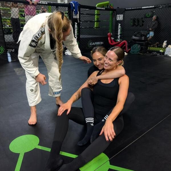 A brown-belt instructor in a white gi teaching two women a Brazilian Jiu-Jitsu grip at Carbon Gym Geelong