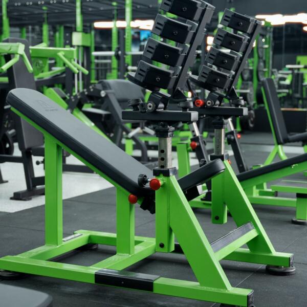 Close-up of a glossy green weight stack cover with the Arsenal Strength logo, hexagon ceiling lights softly blurred behind.