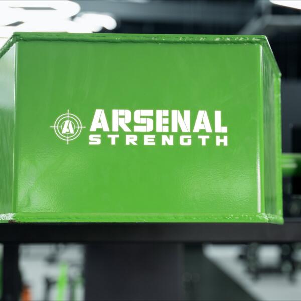 Close-up of a glossy green Arsenal Strength branded weight stack cover, with soft hexagon light glow in the background.