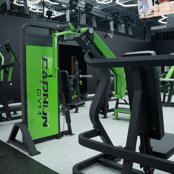 Cable crossover machine with a green branded panel reading CARBON GYM, surrounded by benches and strength equipment.