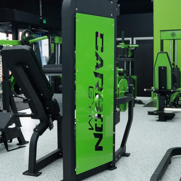 Close-up of a gym machine's green branded panel reading CARBON GYM, with other equipment blurred in the background.