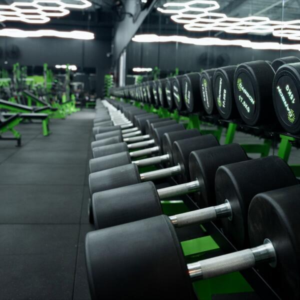 Close-up of black dumbbells labelled with weight and Carbon Gym branding, lined up in rows on a green rack.