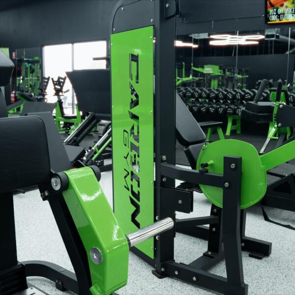 Green and black leg press machine with a CARBON GYM branded panel, surrounded by other strength equipment.