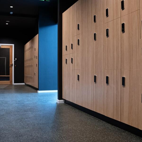 Close-up of wood-veneer lockers with black digital locks, arranged in rows along a hallway wall.