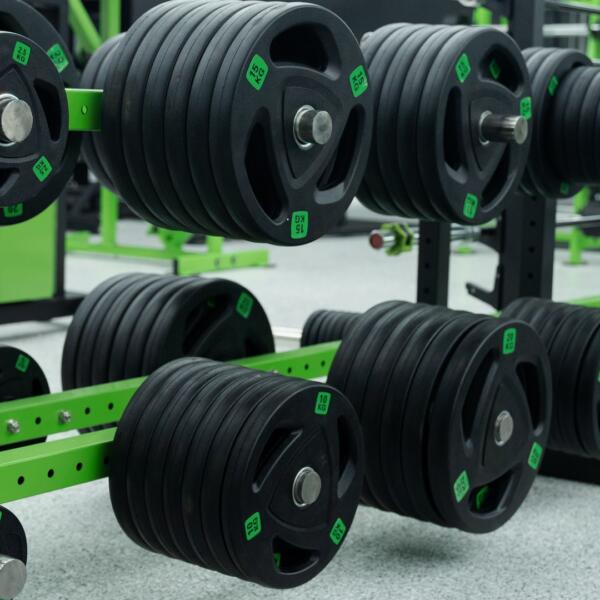 Close-up of stacked black weight plates with green accents mounted on storage pegs in a gym.
