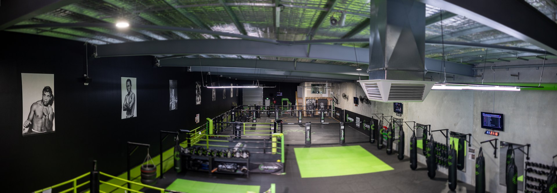 Elevated interior photo of a boxing gym with a ring, rows of hanging heavy bags, and black-and-white boxer portraits on dark walls.