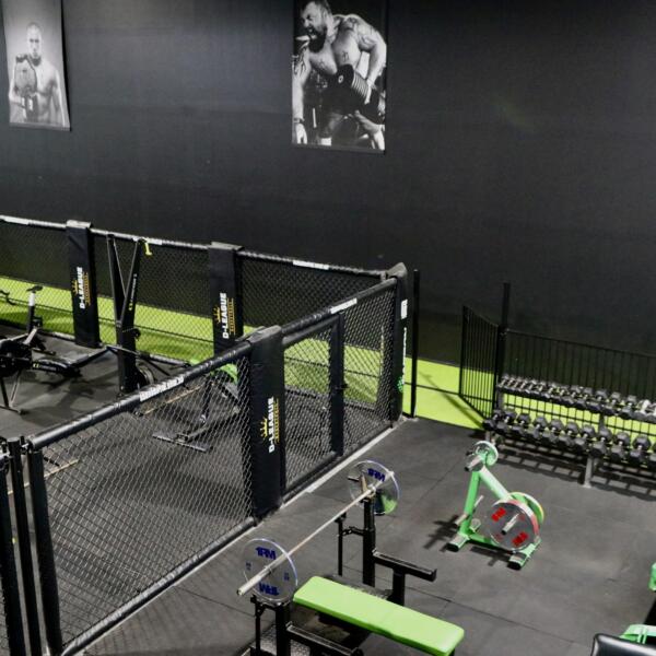 Gym free weights area with dumbbell racks, a flat bench and black-and-white athlete portraits on a dark wall.
