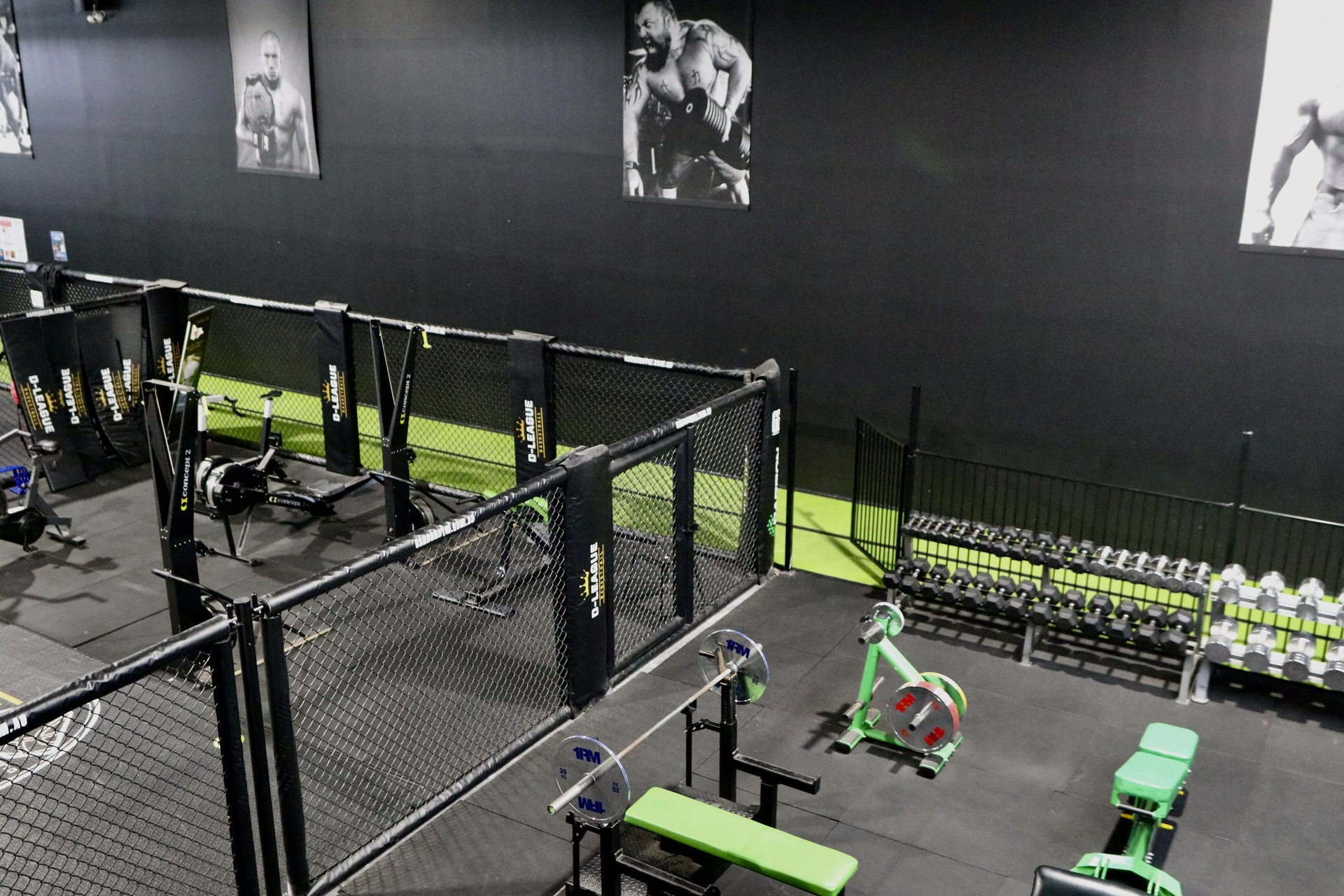 Gym free weights area with dumbbell racks, a flat bench and black-and-white athlete portraits on a dark wall.