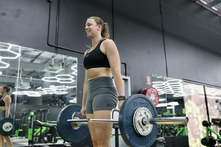 Sara Blicavs smiling while standing with a loaded barbell at Carbon Gym