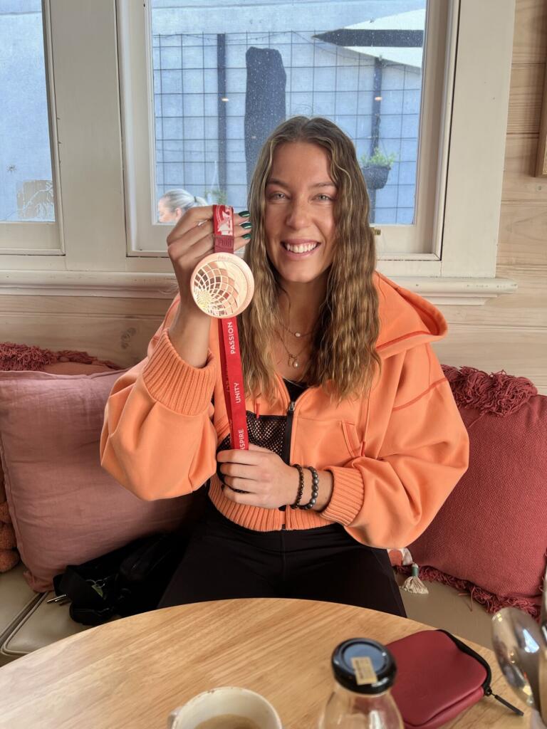 Sara Blicavs smiling and holding up her Olympic medal indoors