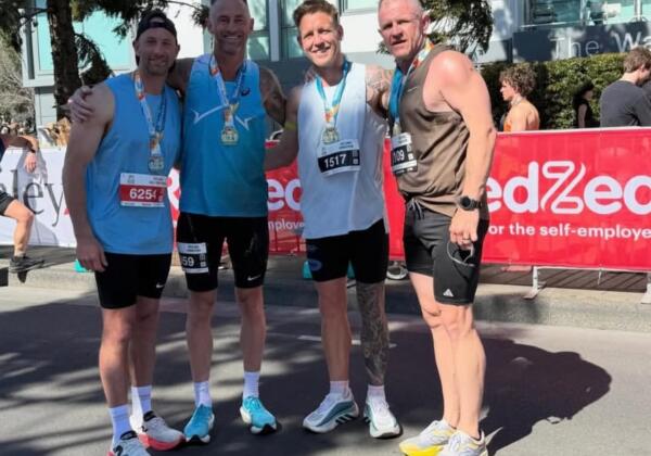 Four runners wearing finisher medals and race bibs stand together at the Geelong Running Festival marathon finish, with Carbon Gym coach Billy Nicholls