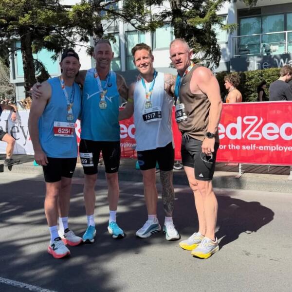 Four runners wearing finisher medals and race bibs stand together at the Geelong Running Festival marathon finish, with Carbon Gym coach Billy Nicholls